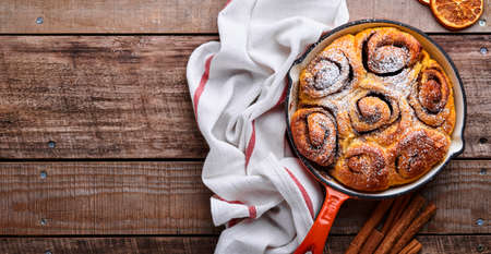 Cinnabon cinnamon rolls buns with pumpkin, nut, caramel and sugar cream iced on rustic wooden background table. Top view. Sweet Homemade Pastry christmas baking. Kanelbule - swedish dessert.の写真素材