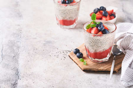 Chia strawberry pudding. Healthy vegan breakfast chia seeds pudding with fresh berries and mint in glass on gray concrete background. Concept of healthy eating, dieting, fitness menu. selective focus.の写真素材
