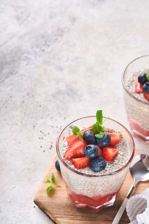 Chia strawberry pudding. Healthy vegan breakfast chia seeds pudding with fresh berries and mint in glass on gray concrete background. Concept of healthy eating, dieting, fitness menu. selective focus.の写真素材