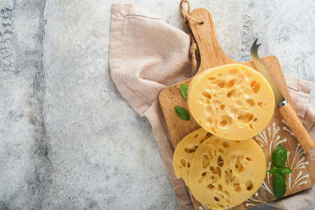 Cheese Maasdam or Radamer. Piece of cheese on wooden standa on old gray concrete background. top view. Free space for your text.の写真素材