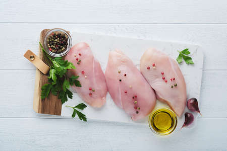 chicken breast. Two Chicken fillet with spices, olive oil and parsley on white stone cutting board on white wooden table background. Top view with copy space. Food meat cooking background.の写真素材