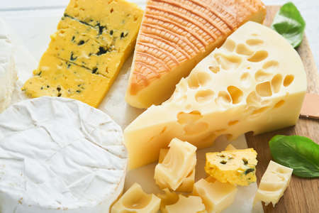 Piece of maasdam cheese and camembert, smoked cheese, blue cheese, parmesan, brie cheese with basil...