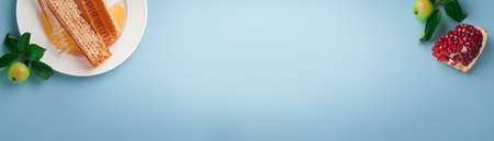 Rosh Hashanah. Honey jar, honeycomb, apple and pomegranate on simple blue background. Jewish New Year holiday greeting card. Rosh Hashanah holiday attributes. Space for text. Banner.の写真素材