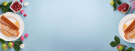 Rosh Hashanah. Honey jar, honeycomb, apple and pomegranate on simple blue background. Jewish New Year holiday greeting card. Rosh Hashanah holiday attributes. Space for text. Banner.の写真素材