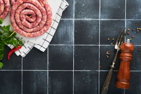 Raw spiral pork sausages. Fresh pork sausages tasty twisted spiral for bbq on white stand with spices and herbs for Octoberfest party dinner on gray background. top view. Oktoberfest set.の写真素材