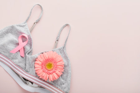Pink Breast Cancer Awareness Ribbon. Gerbera and pink ribbon tape lying on female white bra on backgrounds. Breast cancer awareness and October Pink day, world cancer day. top view. Mock up.の写真素材