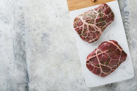 Steak Raw. Raw cowboy steak, marbled beef meat with spices rosemary and pepper on white marble slate and gray table background. top view. Mock up.の写真素材