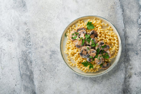 Fusilli pasta with mushrooms, cheese and garlic creamy sauce on plate on gray stone or concrete table background. top view. Traditional Italian food.の写真素材