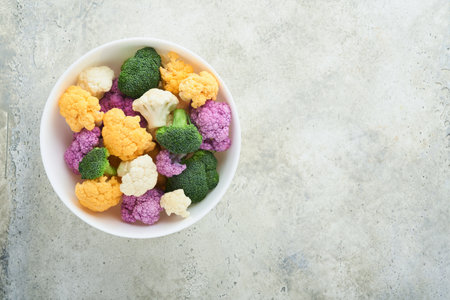 Colorfu cauliflower. Cauliflower cut into small pieces white bowl on light stone marble concrete background. Purple, yellow, white and green color cabbages. agricultural harvest. Mock up. top view.の写真素材