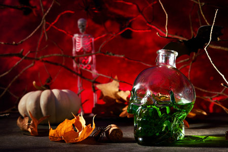 Halloween green cocktail. Halloween cocktail glass goblet for Halloween and bottle form skull on red dark backgrounds. Halloween party with candy eyes, bats, spiders. Dia de los Muertos. Clous up.の写真素材