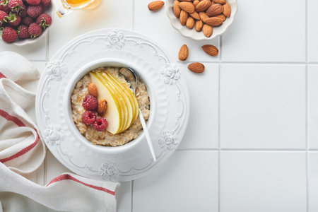 Oatmeal. Bowl of oatmeal porridge with raspberry, pear and honey on gray concrete old table background. Hot and healthy food for breakfast, top view, flat layの写真素材