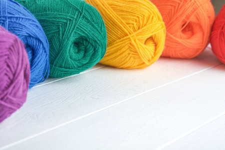 Many multi-colored balls of threads on knitted fabric on white wooden backgrounds. Yarn of bright...