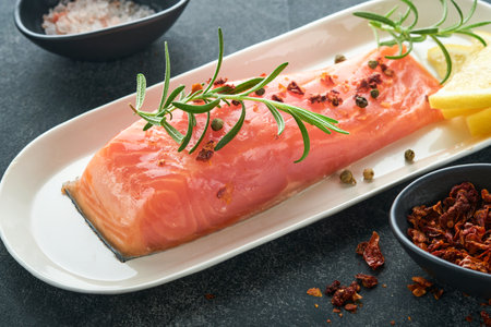 salmon fish piece. Fresh raw salmon fish piece on marble board stand with herbs and lemon on black...