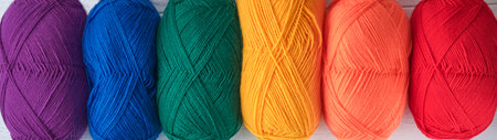 Many multi-colored balls of threads on knitted fabric on white wooden backgrounds. Yarn of bright...