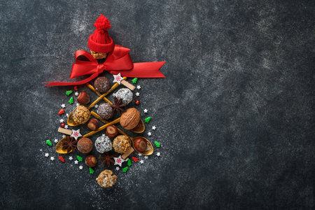 Christmas tree made of chocolate truffles, hazelnuts, anise stars, decorations, spoons and powdered sugar snow on dark background. Christmas holiday card. Holiday food concept for magazine page.の写真素材
