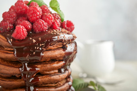 Chocolate Pancakes. Pancakes with fresh raspberry with chocolate glaze or toppings in gray bowl on light gray table background. Homemade classic american pancakes. Page for magazine concept.の写真素材
