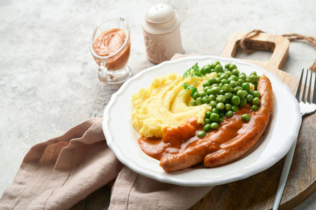 Bangers and mash. Grilled sausages with mash potato and green pea on white plate on grey background. Traditional dish of Great Britain and Ireland. BBQ beef sausages. Top view.の写真素材