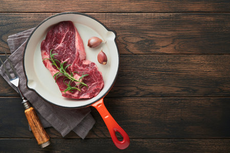 Raw beef steak. Raw fresh Ribeye steak with rosemary, salt and pepper in iron pan on cutting board on dark concrete background. Raw beef steak and spices for cooking.の写真素材