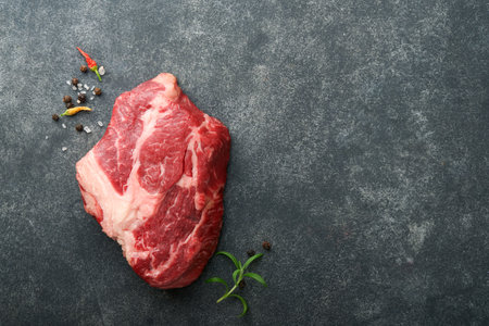 Raw beef steak. Raw fresh Chuck roll steak with rosemary, salt and pepper on cutting board on dark concrete background. Raw beef steak and spices for cooking.の写真素材