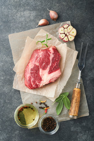 Raw beef steak. Raw fresh Chuck roll steak with rosemary, salt and pepper on cutting board on dark concrete background. Raw beef steak and spices for cooking.の写真素材