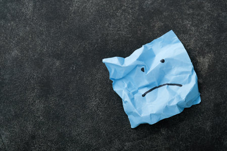 Blue crumpled sticky notes blank with drawing sad face on black background with copy space ready for your message. Blue Monday and mental health concept idea. Flat lay copy space on black background.の写真素材