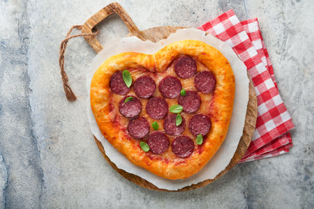 Valentines day heart shaped pizza with mozzarella, pepperoni and basil, wine bottle, two wineglass, gift box on light gray background. Idea for romantic dinner Valentines day. top view. Mock up.の写真素材