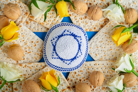 Passover celebration concept. Blue Star of David made from matzah, white and yellow roses, kippah...