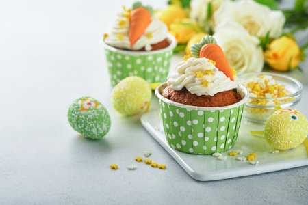 Carrot cake cupcakes for Easter. Carrot cupcakes with cream cheese frosting decorated with tiny marzipan carrots on white background. Happy Easter and spring holiday concept. Holydays homemade dessertの写真素材