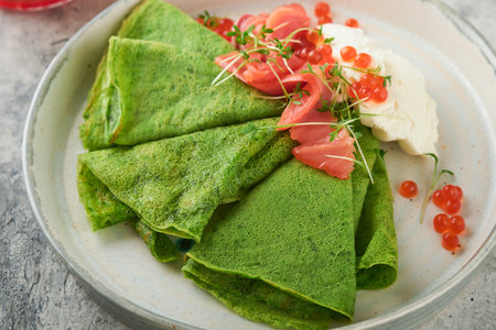 green pancakes. Round thin green spinach crepe pancakes with red and black caviar and yogurt sauce on gray concrete background. Healthy vegan breakfast. National Pancake Day or Fat Tuesday Day.の写真素材