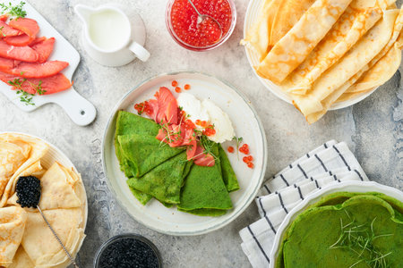 Green and white pancakes assorted. Thin green spinach and white crepe pancakes with red and black caviar, sauce on gray concrete table background breakfast. National Pancake Day or Fat Tuesday Day.の写真素材