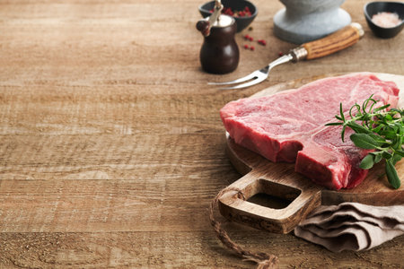 Thick Raw T-Bone Steak. Dry-aged Raw T-bone or porterhouse beef meat Steak with herbs and salt on dark background. Selective focus and copy space.の写真素材