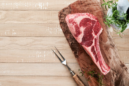 Fresh tomahawk raw steak. Dry aged raw tomahawk beef steak with herbs and salt on old wooden background. Preparing to grill. Top view and copy space.の写真素材