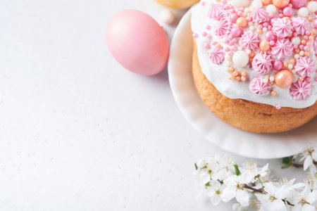 Traditional Easter sweet bread or cakes with white icing and sugar decor, colored eggs and cherry blossom tree branch over white table. Various Spring Easter cakes. Happy Easter day. selective focus.の写真素材
