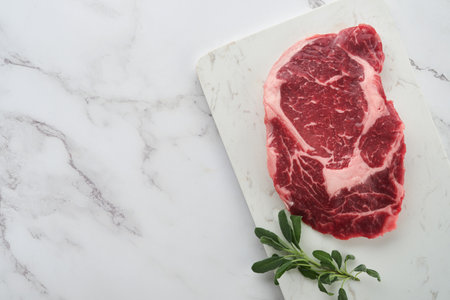 Raw fresh ribeye steak or Rib-eye steak. Raw fresh marbled meat Ribeye Black Angus and seasonings pepper, rosemary, thyme and salt on old wooden rustic background. Top view and copy space.の写真素材