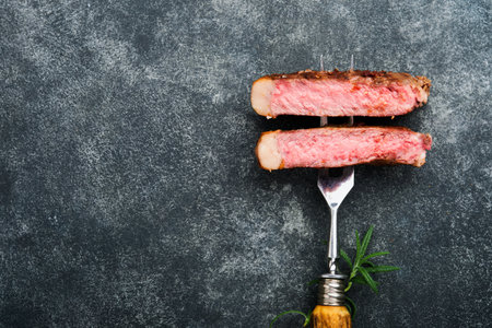Steaks T-bone. Slices of beef grilled meat barbecue steak on meat fork on burned dark wooden background with copy space for your text. top view. Mock up.の写真素材
