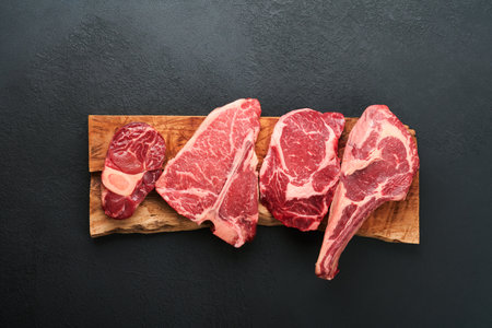 Raw prime steaks. Variety of fresh black angus prime meat steaks T-bone, New York, Ribeye, Striploin, Tomahawk cutting board on black or dark background. Set of various classic steaks. top view.の写真素材