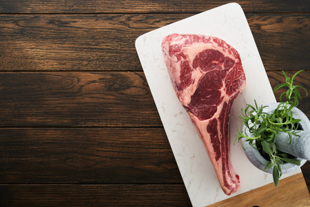 Fresh tomahawk raw steak. Dry aged raw tomahawk beef steak with herbs and salt on old wooden background. Preparing to grill. Top view and copy space.の写真素材