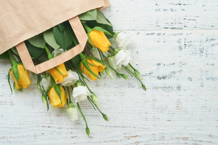 Easter concept. Bouquet of fresh white and yellow roses in paper bag on old white wooden background. Passover Pesah celebration concept. Concept of mothers day, womens day, spring background. top viewの写真素材