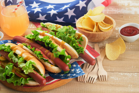 4th of July American Independence Day traditional picnic food. Hot dog with potato chips and cocktail, American flags and symbols of USA Patriotic picnic holiday on wooden background. top view.の写真素材