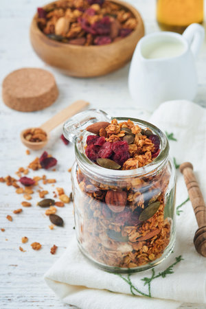 Homemade granola in glass jar with greek yogurt or milk and cashews, almonds, pumpkin with dried cranberry seeds in on white rustic wooden table background. Healthy energy breakfast or snack. top viewの写真素材