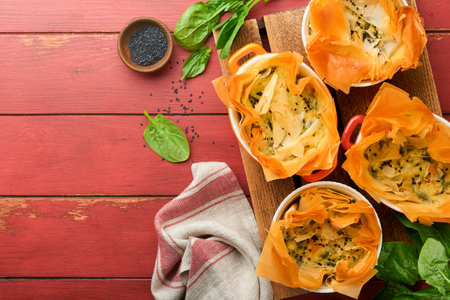 Filo pies with soft feta cheese and spinach in ceramic molds on old red wooden table backgrounds....
