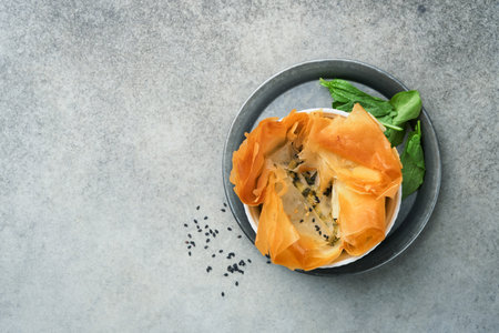 Filo pies with soft feta cheese and spinach in ceramic molds on old gray table background. filo portions pies. Small Baked Spanakopita pies. top view. copyspace. Traditional Greek cuisine.の写真素材