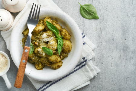 Potato gnocchi. Traditional homemade potato gnocchi with sauce pesto and basil in white plate on kitchen table on light gray kitchen table background. Traditional Italian food. top view.の写真素材