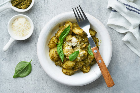Potato gnocchi. Traditional homemade potato gnocchi with sauce pesto and basil in white plate on kitchen table on light gray kitchen table background. Traditional Italian food. top view.の写真素材
