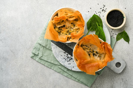 Filo pies with soft feta cheese and spinach in ceramic molds on old gray table background. filo...