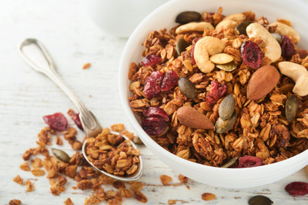 Homemade granola in glass jar with greek yogurt or milk and cashews, almonds, pumpkin with dried cranberry seeds in on white rustic wooden table background. Healthy energy breakfast or snack. top viewの写真素材