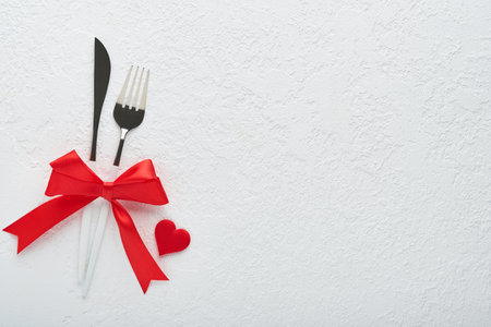 Valentines day romantic table setting. Empty or closeup of a dinner black plate, knife, fork and decorative silk hearts on white background. holiday concept. Copy space for inscriptions.の写真素材