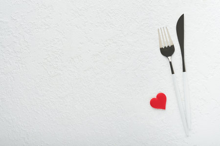 Valentines day romantic table setting. Empty or closeup of a dinner black plate, knife, fork and decorative silk hearts on white background. holiday concept. Copy space for inscriptions.の写真素材