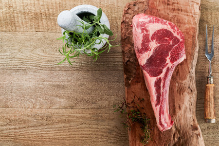 Fresh tomahawk raw steak. Dry aged raw tomahawk beef steak with herbs and salt on old wooden background. Preparing to grill. Top view and copy space.の写真素材