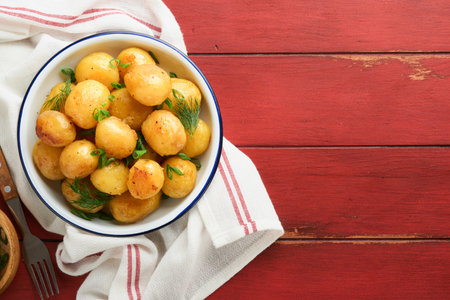 Fresh boiled new or young potatoes with butter, fresh dill and onions in white bowl on old red rustic wooden background. Tasty new boiled potatoes. top view.の写真素材